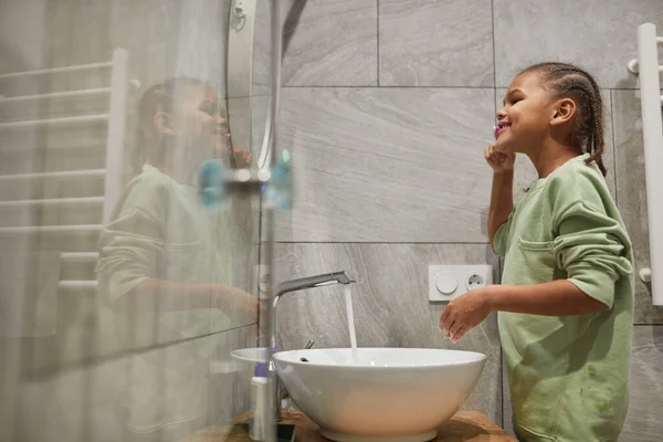 Saçları Örgülü Banyoda Aynayla Dişlerini Fırçalayan Mutlu Zenci Çocuk Portresi — Stok fotoğraf