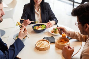 Cafe 'deki iş yemeği sırasında Asya yemeklerinin keyfini çıkaran dört kişinin yüksek açılı görüntüsü.