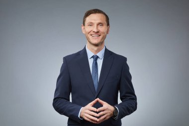 İş elbisesi giymiş yetişkin beyaz bir adamın belden yukarı portresi. Stüdyoda gri arka planda dururken kameraya gülümsüyor.