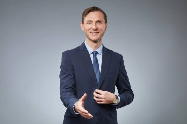 Gülümseyen beyaz iş adamının belini kaldırıp el sıkışmak için kameraya uzanırken gri arka planda durup, boşluğu kopyala