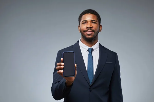 Stock image Portrait of smiling black businessman holding blank smartphone mockup and showing to camera with grey background, copy space