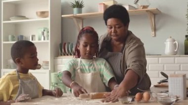 9 yaşındaki Afrikalı Amerikalı kız ve erkek kardeşi mutfaktaki sevgili büyükannelerine el yapımı hamuru sarmalarında yardım ediyorlar.