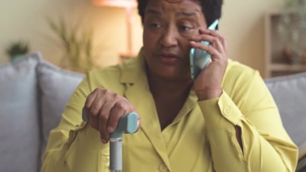 坐在客厅沙发上 拿着手杖在智能手机上聊天的非洲裔美国老年妇女 — 图库视频影像