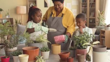 Önlüklü iki Afro-Amerikan ergen çocuk büyükannelerine ev bitkilerini toplamada yardım ediyor.