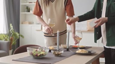 Romantik eşcinsel çift evde yıldönümü yemeği yiyor, mutfak masasında mum yakıyor ve beyaz şarap bardaklarını tokuşturuyor.