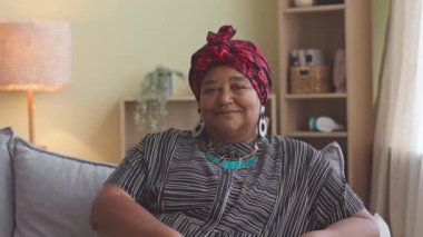 Modern Afrikalı Amerikalı son sınıf öğrencisi kameraya poz veriyor oturma odasında rahat bir koltukta oturuyor ve gülümsüyor.