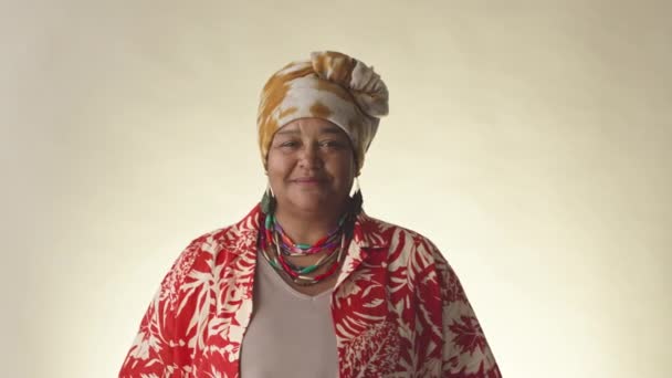 身着头巾和夏威夷印花衬衫的快乐而成熟的黑人女性的中肖像画 站在清晰的摄影棚背景上 对着镜头微笑 — 图库视频影像