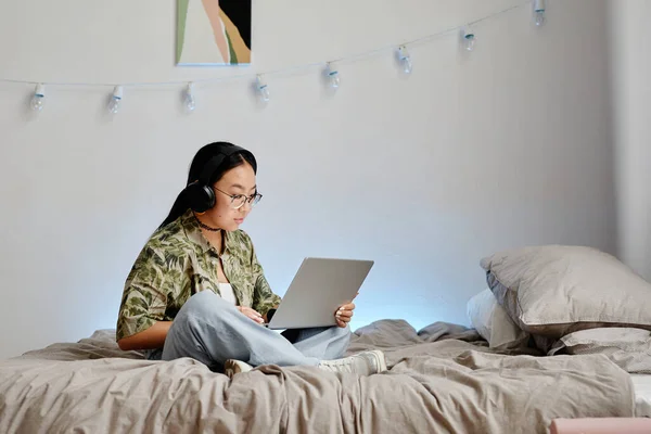 Minimalna Długość Portretu Azjatyckiej Nastolatki Używającej Laptopa Słuchawkami Siedzącej Łóżku — Zdjęcie stockowe