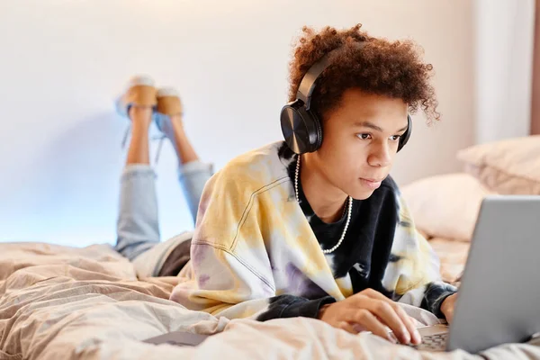 Portret Nastoletniego Czarnego Chłopca Korzystającego Komputera Leżącego Łóżku Minimalnym Pomieszczeniu — Zdjęcie stockowe
