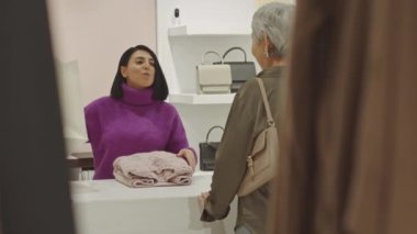 Çağdaş Asyalı yetişkin kadın lüks tasarımcı galerisinden kıyafet alıyor. Beyaz tezgahın yanında duruyor.