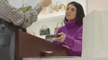 Çağdaş bir kadın lüks bir butikte kıyafetlerin parasını öderken cüzdanından kredi kartını çıkarıyor.
