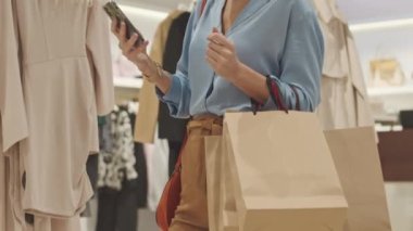 Zarif sarışın beyaz kadın portresini yukarı kaldır. Elinde kağıt alışveriş torbalarıyla akıllı telefondan mesaj atıyor. Tasarımcı butiğinde alışveriş yapıyor.