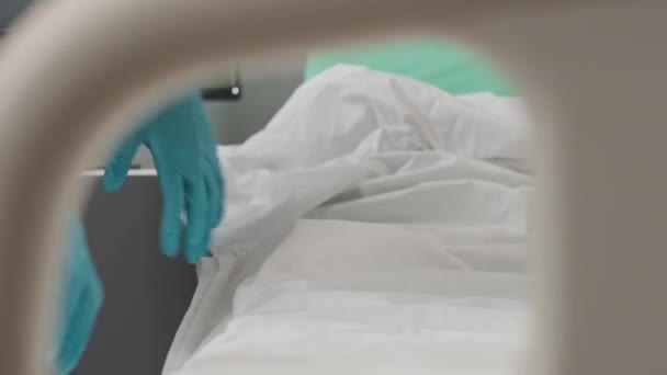 新しい患者のためにそれを準備しながら 病院区のベッドに新鮮な白いベッドシートを敷く認識できない手袋の看護師 — ストック動画