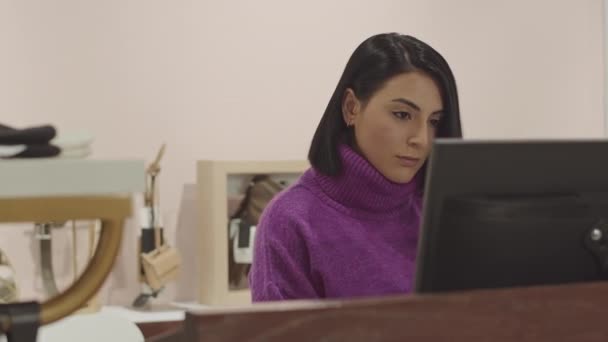 穿着紫罗兰色龟颈毛衣的年轻漂亮黑发中东时装设计师在她的精品店电脑显示器上查看销售信息 — 图库视频影像