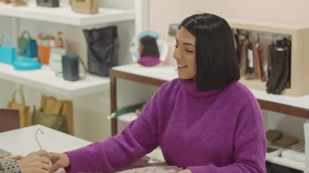 柜台上的年轻女店员在设计师陈列室与正在购买毛衣的当代金发女人交谈 — 图库视频影像