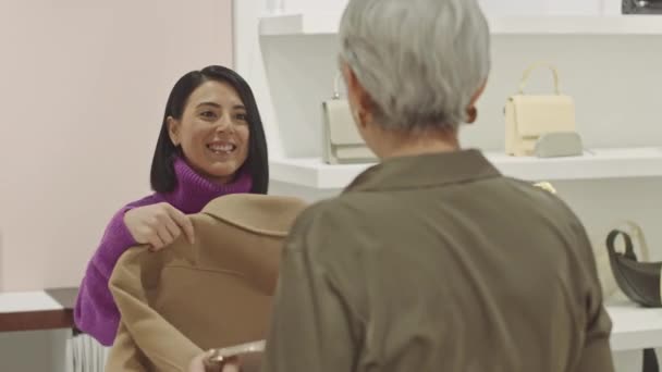 在设计师陈列室工作的年轻中东女性售货员在柜台边包装物品时与顾客交谈 — 图库视频影像