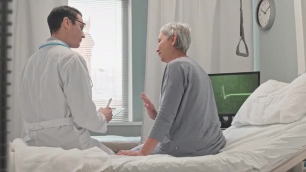 Jovem Médico Masculino Jaleco Branco Visitando Mulher Asiática Madura Enfermaria — Vídeo de Stock