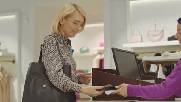 Mulher Loira Elegante Pagando Com Smartphone Enquanto Compra Roupas Boutique — Vídeo de Stock