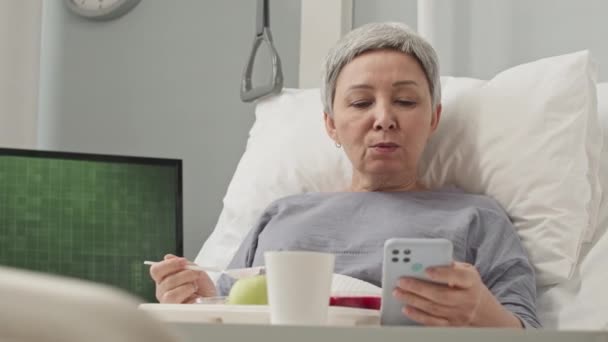 亚洲妇女在医院的病床上吃早餐时使用智能手机 术后康复 — 图库视频影像