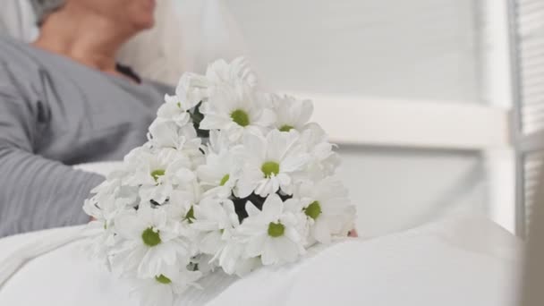 病気の母親を病院で訪ねるために育った息子のクロップショット 白い病院のベッドに横たわる花の花束 — ストック動画