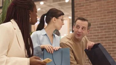 Alışveriş merkezinde birlikte alışveriş yaptıktan sonra alışverişlerini gösteren üç farklı etnik arkadaş.