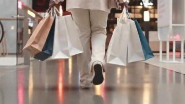 Seçkin beyaz takım elbiseli, elinde bir sürü kese kâğıdıyla modern alışveriş merkezinde elinde yemek çantasıyla gezen, tanınmamış bir kadının alçak görünümü.