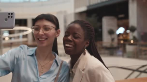 两个多民族快乐的女孩一边拿着购物袋 一边用智能手机自拍照 在现代购物中心一起购物 — 图库视频影像