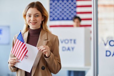 Seçim günü oy kullanma merkezinde Amerikan bayrağı tutan gülümseyen genç kadının belindeki portre, boşluğu kopyala