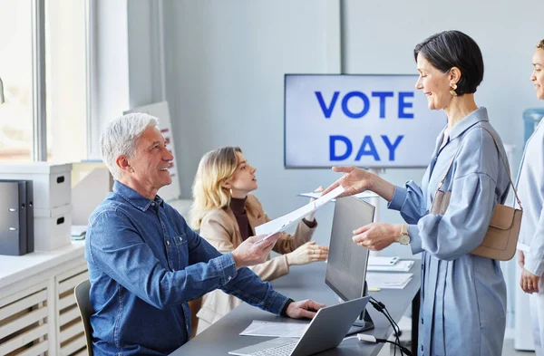 Side view portrait of smiling adult woman taking ballot form while voting on election day, copy space