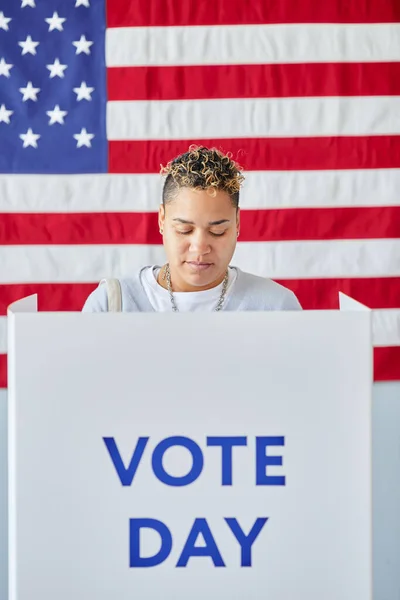 アメリカの国旗に反対する選挙の日に投票ブースに立っている若い黒人女性の垂直の肖像画 — ストック写真