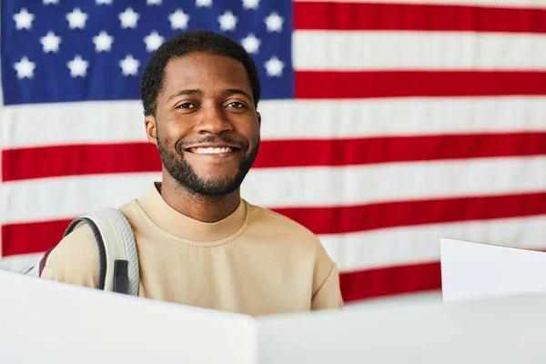 Portrait of smiling black man voting against USA banner background, copy space