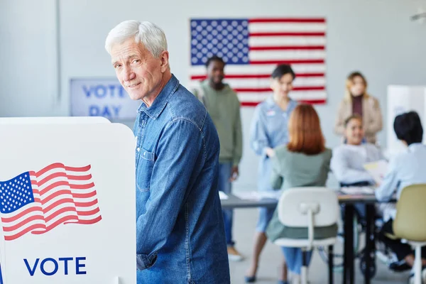 stock image Side view portrait of smiling senior man voting in booth on election day and looking at camera, copy space