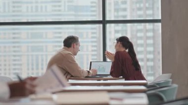 Birkaç meslektaşım kafenin panoramik penceresine karşı masada oturmuş laptop ekranında iş grafiğini inceliyor.