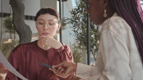 Két Fiatal Változatos Kolléganő Akik Üzleti Dokumentumokról Beszélgetnek Miközben Kávézóban — Stock videók