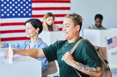 Gülümseyen Amerikalı kadının seçim günü oy kullanma ve oy pusulasını çöpe atmasının yan görünümü