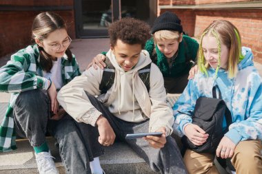 Okullarında basamaklarda oturan bir grup genç derslerden sonra video içeriği izlemek için akıllı telefon kullanıyor.