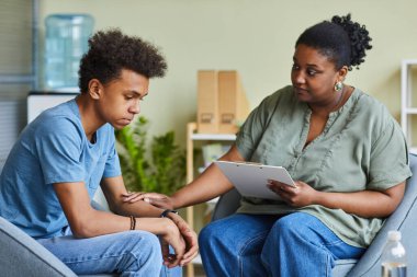 African psychologist supporting depressed teenage boy feeling guilty about behavior during therapy at office clipart