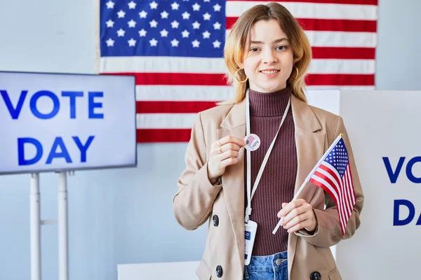 私が投票所に立っている間 私はステッカーとアメリカの旗に投票する笑顔の若い女性を待って コピースペース — ストック写真