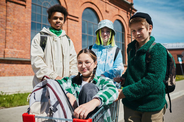 Portrait of group of teen boys and girls looking at camera while riding on shopping cart on the street