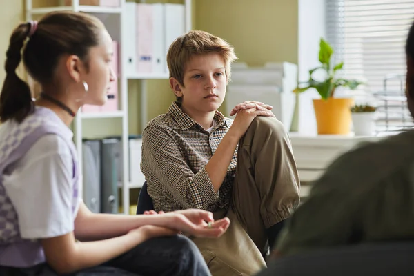Difficult kid sitting on chair and listening to other children during group of psychotherapy session