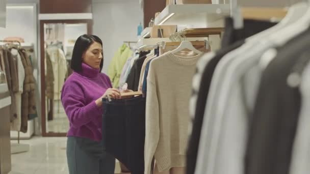 穿着紫色龟颈毛衣的年轻中东女售货员在设计师陈列室的衣架上贴上销售标签 — 图库视频影像