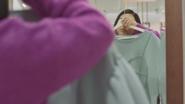 Orta Doğulu genç bir kadın lüks bir butikte aynanın önünde tasarımcı kıyafetleri deniyor.