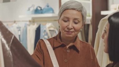 Mağaza danışmanı, olgun Asyalı kadınların modern tasarımcı mağazasında kıyafet seçmelerine yardım ediyor.