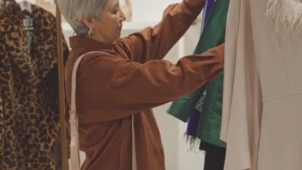 Κομψό Ώριμη Ασιάτισσα Γυναίκα Επιλέγει Ρούχα Για Αγοράσει Κρέμονται Ράφι — Αρχείο Βίντεο