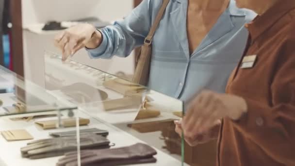 优雅的金发女人让售货员从设计师商店橱窗里的玻璃橱窗里拿出皮革护身符 — 图库视频影像