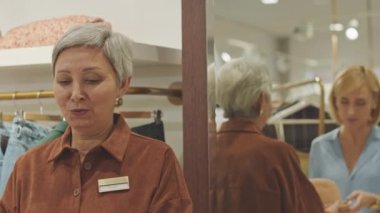 Dükkan danışmanının yardımıyla şık sarışın kadın özel tasarım butikte şapka seçip deniyor.