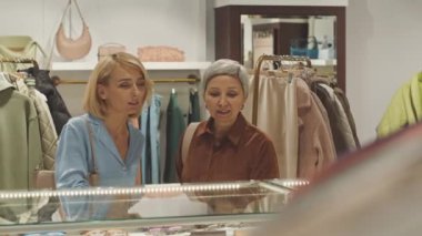İki zarif modern kadın cam tezgâha bakıyor ve pahalı bir butikte alışveriş yaparken eşyaları tartışıyor.