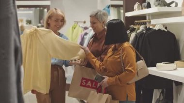 Çağdaş tasarımcı galerisinde üç farklı kadın birlikte kıyafet alışverişi yapıyor.