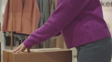 Tasarımcı butikte çalışan, karton kutunun içindeki eşyaları boşaltan tanınmayan kadın tezgahtarın görüntüsü.