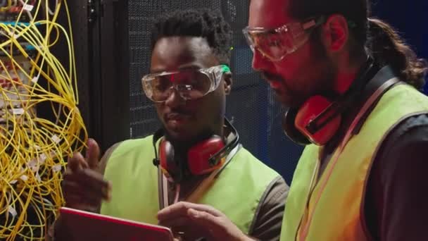Två Multietniska Manliga Ingenjörer Skyddsglasögon Och Hörlurar Kontrollerar Kablar Serverrummet — Stockvideo